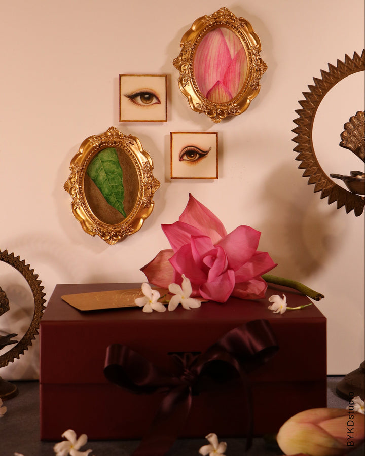 Decorative wall with gold-framed artworks and a pink flower on a red box.