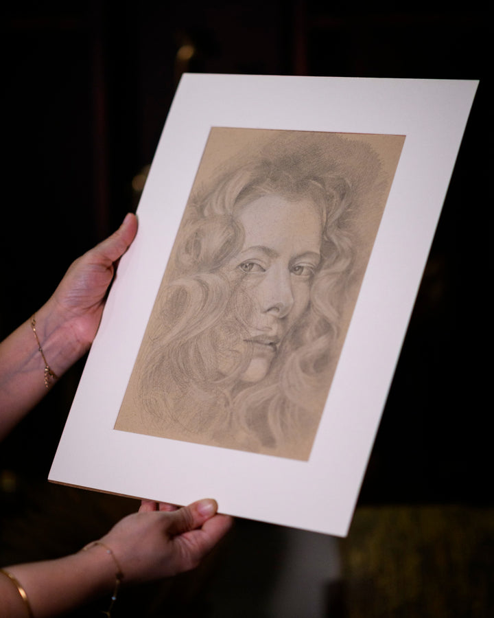 Person holding a framed portrait drawing of a woman with long hair on a dark background