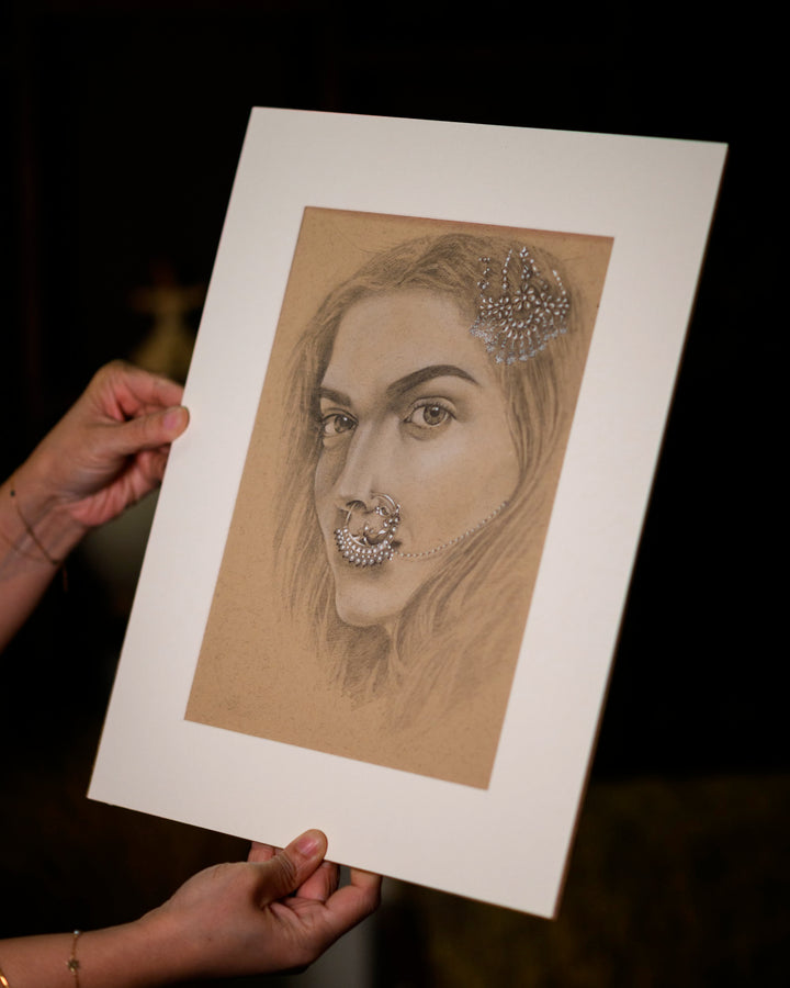 Person holding a framed drawing of a woman's face with jewelry on a dark background